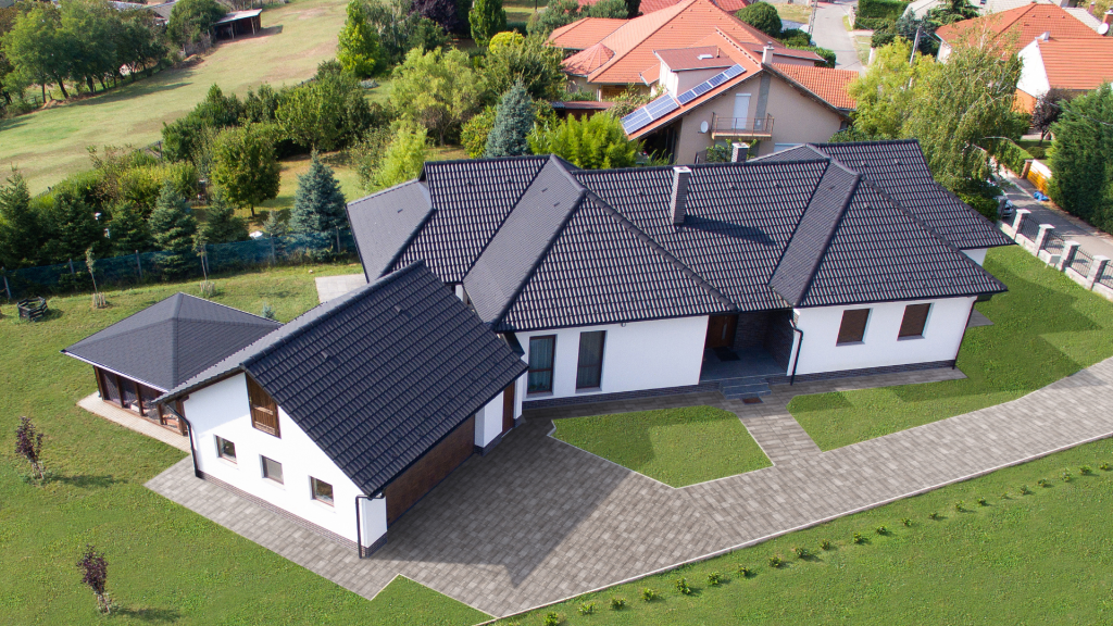 Fekete Synus tetőcseréppel fedett családi ház Hernádkő Agyag térkővel burkolt környezetben, zöld gyeppel, harmonikus kerttel. Fekete Synus tetőcserép Hernádkő Agyag térkővel párosítva, zöld gyeppel, harmonikus kerttel.