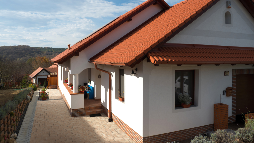 Tégla színű Synus tetőcseréppel fedett családi ház Zselickő széna térkővel burkolt környezetben, zöld gyeppel, harmonikus kerttel. Tégla színű Synus tetőcserép Zselickő széna térkővel párosítva, zöld gyeppel, harmonikus kerttel.
